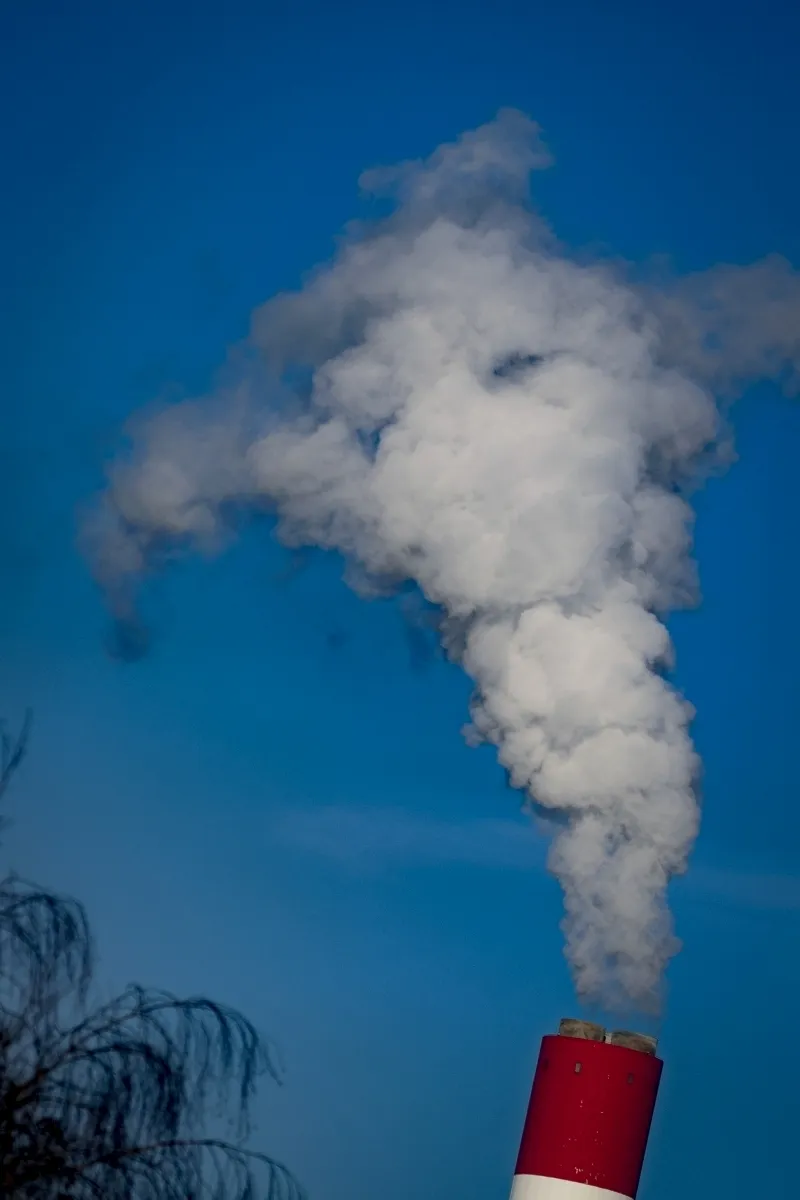 White steam billowing from a red chimney into a clear blue sky